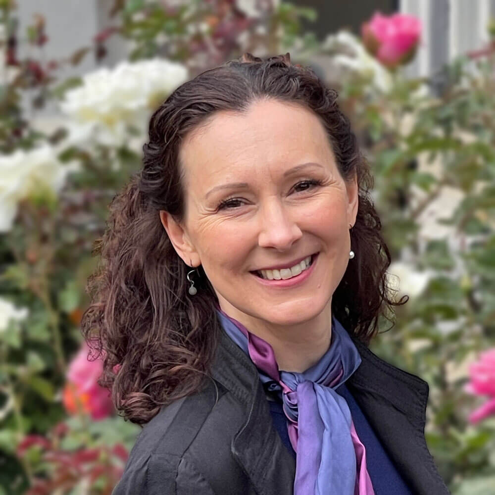 Close-up of Isla Waite, caucasian woman with long dark curly hair wearing a dark indigo-purple top with a blue and purple scarf.