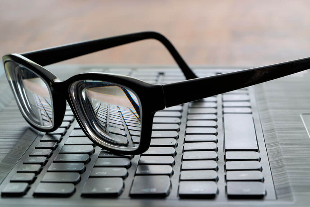 Close up of a pair of black-rimmed glasses sitting on a computer keyboard.